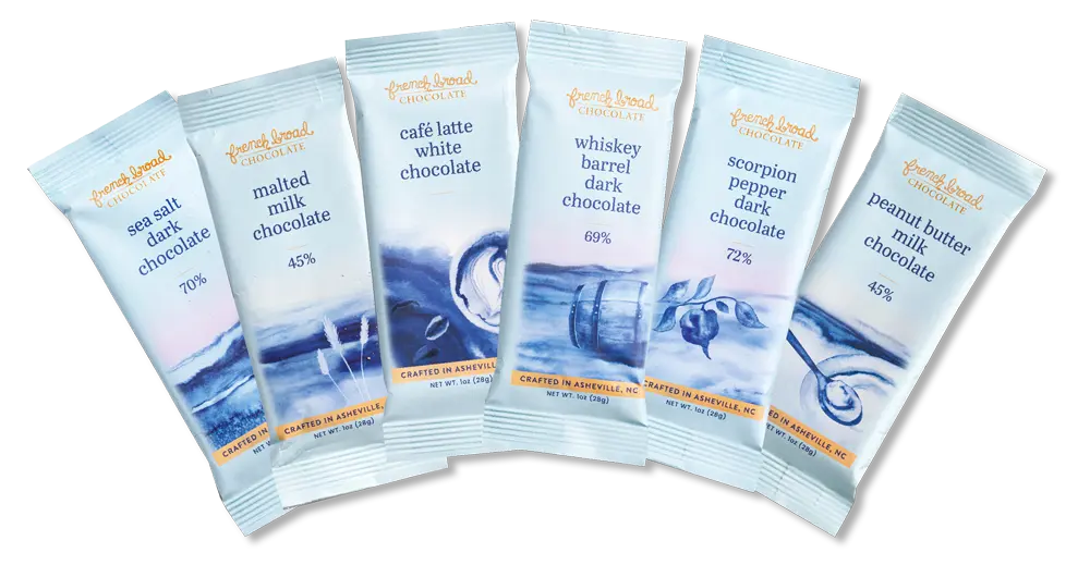Assorted French Broad Chocolate bars in compostable wrappers featuring sea salt dark, malted milk, café latte white, whiskey barrel dark, scorpion pepper dark, and peanut butter milk chocolate flavors
